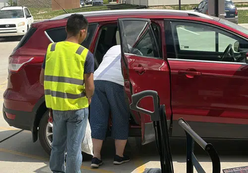 Young man helps woman unload her donations from her vehicle.